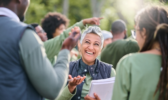 Women holding a clipboard and talking to people around her.