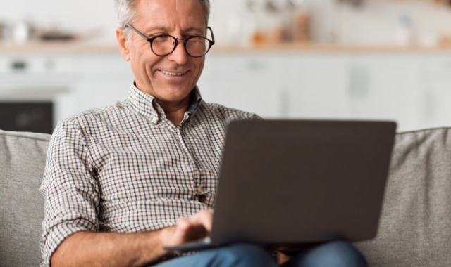 Older man sitting on the couch looking at a laptop.